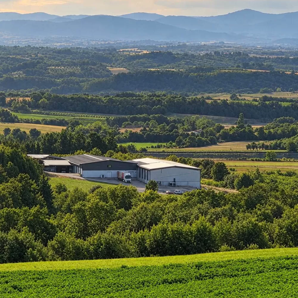 Les bâtiments de l'exploitation Izier au milieu des collines boisées de la Drôme, montagnes à l'horizon